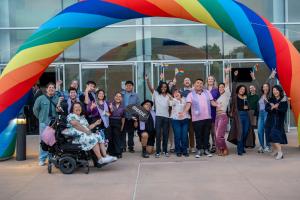 Students, faculty, and staff celebrate under a rainbow arch 